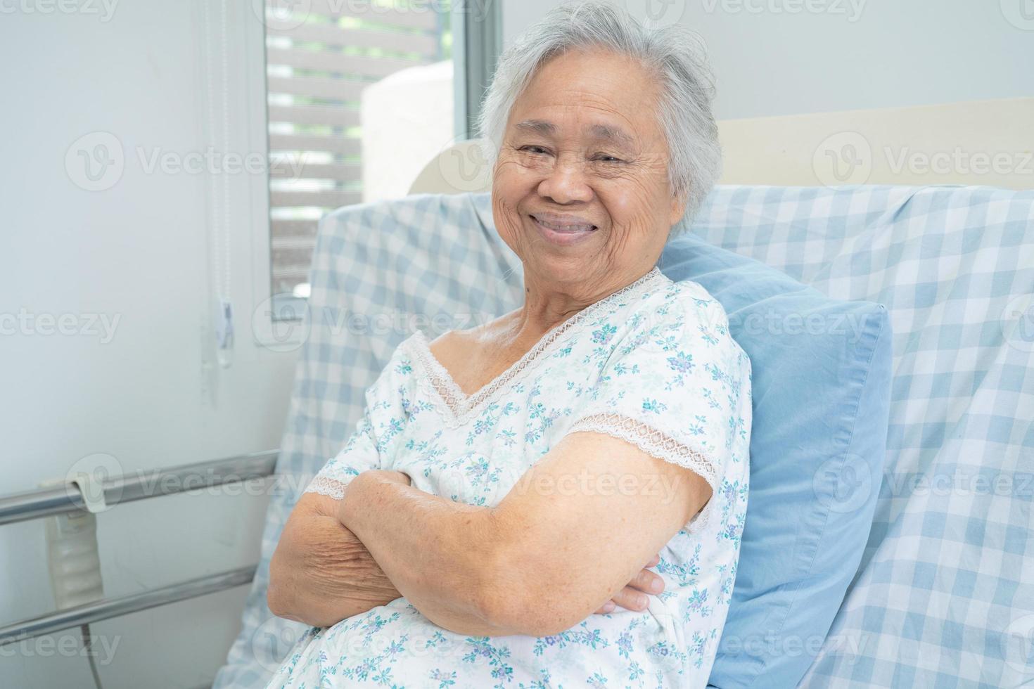 Une patiente asiatique âgée ou âgée d'une vieille dame sourit au visage brillant alors qu'elle est assise sur son lit dans une salle d'hôpital de soins infirmiers, concept médical solide et sain. photo