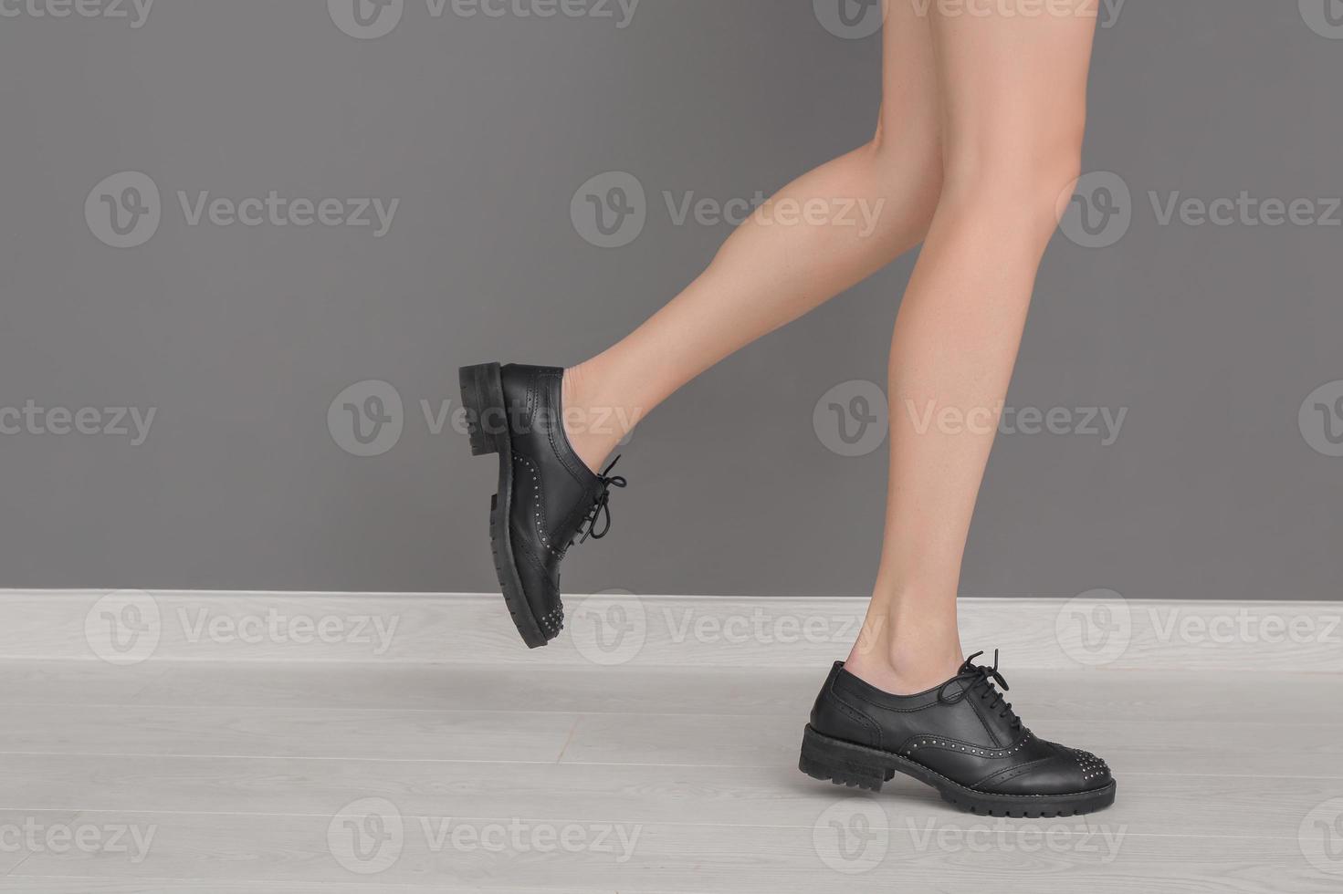 jambes de jeune femme dans des chaussures élégantes debout près du mur gris photo