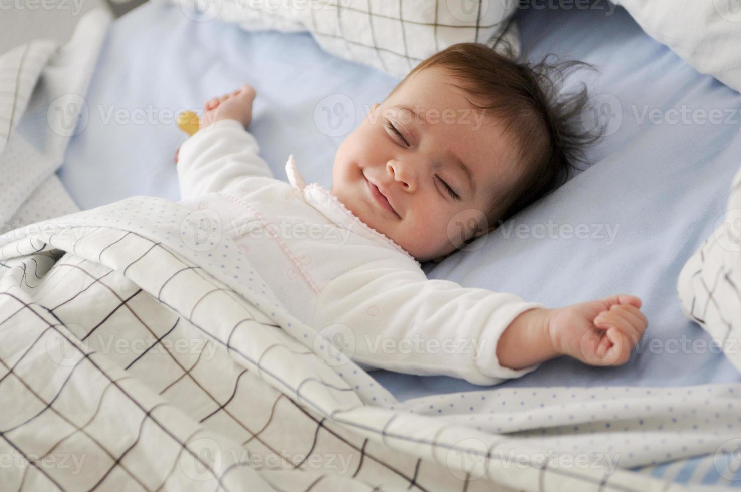 petite fille souriante allongée sur un lit dormant sur des draps bleus photo