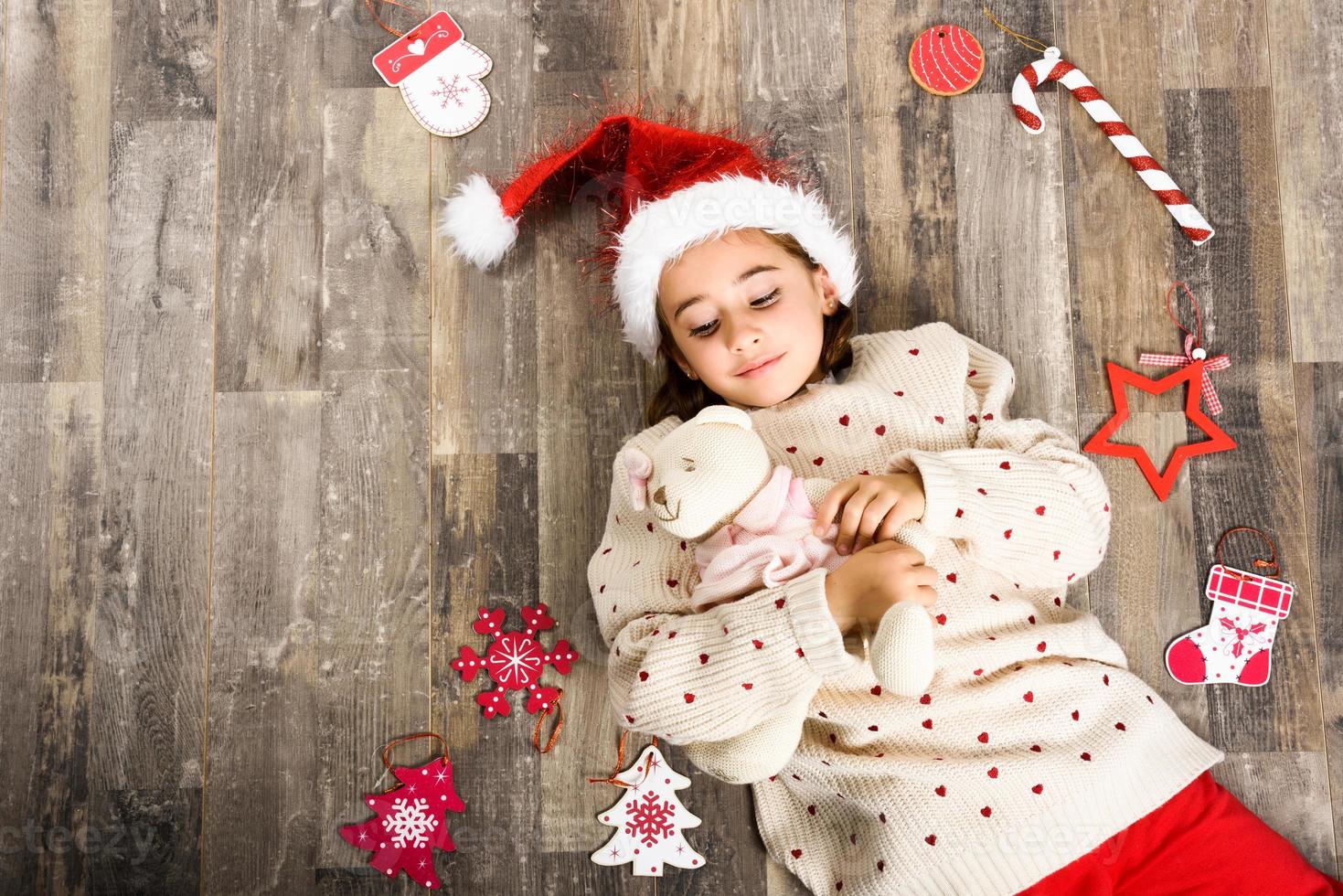 Adorable petite fille portant un bonnet de noel allongé sur un plancher en bois photo