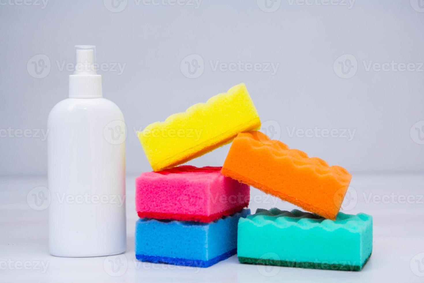 éponges multicolores pour laver la vaisselle et bouteille en plastique sur une table blanche photo