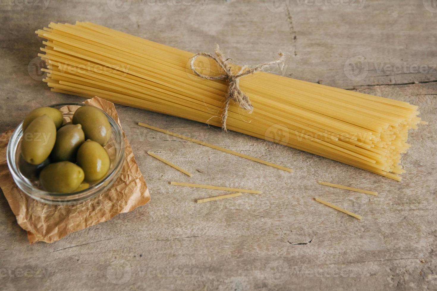 longs spaghettis crus jaunes et olives vertes dans un bol en verre sur fond de bois photo