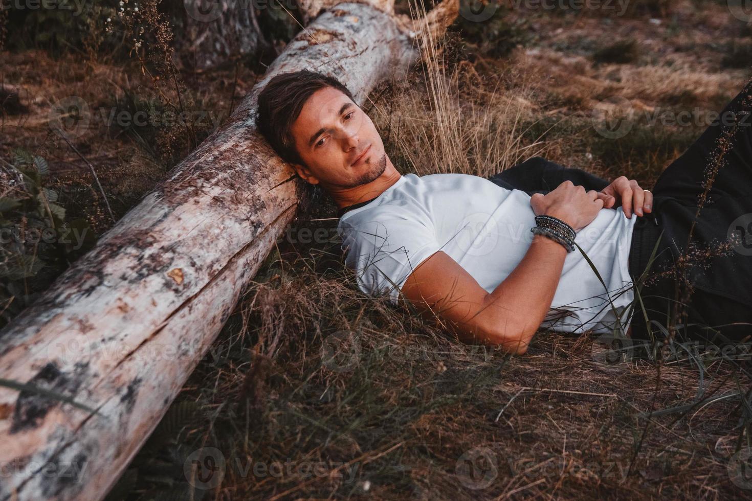 l'homme est allongé sur l'herbe, reposant sa tête sur une bûche au milieu de la forêt relaxante photo