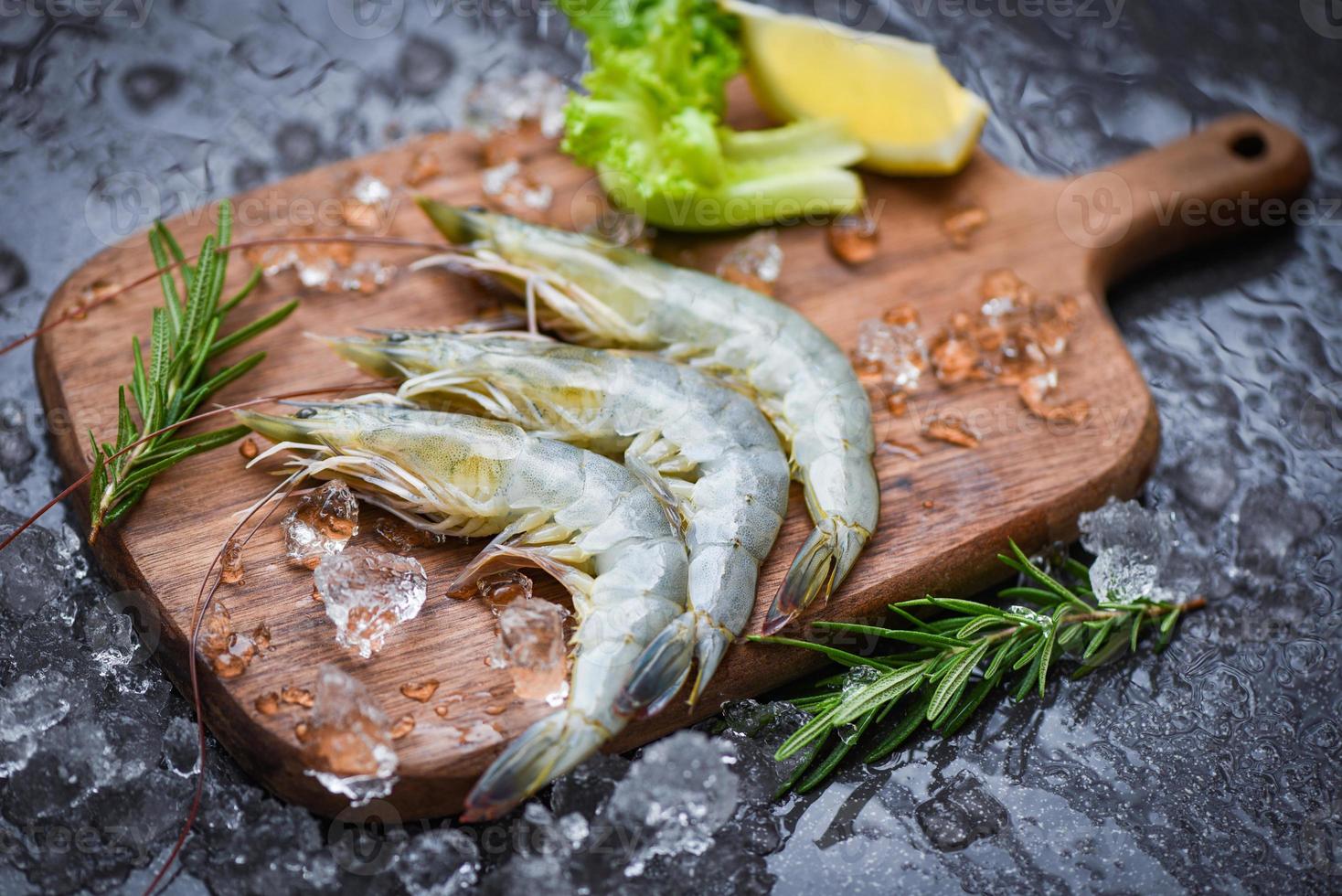 crevettes fraîches sur une planche à découper en bois avec des ingrédients de romarin herbes et épices pour la cuisson des fruits de mer - crevettes crues crevettes sur glace congelées au restaurant de fruits de mer photo
