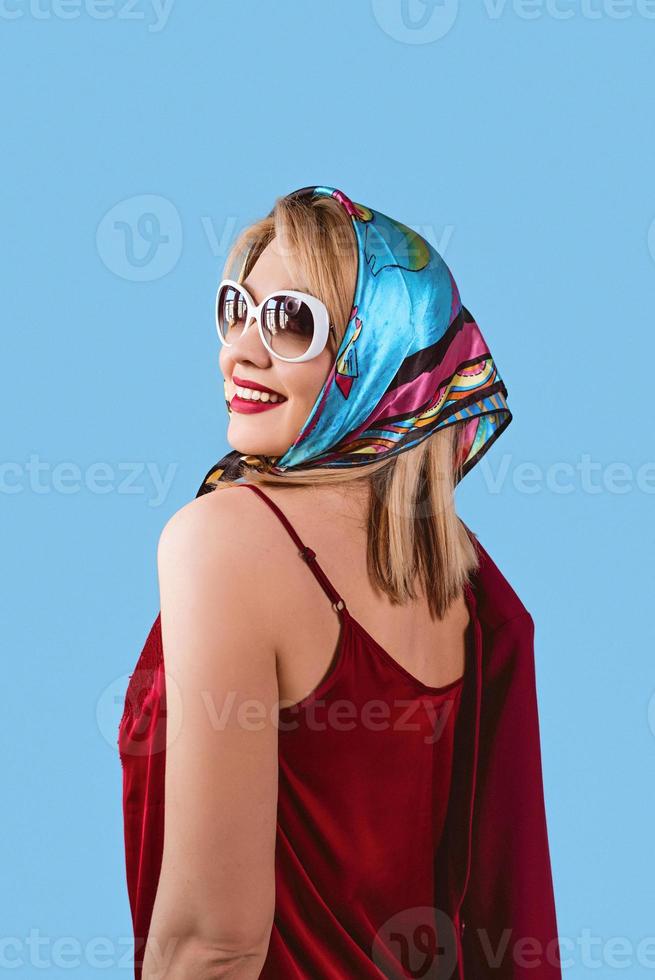 élégante femme blonde fantaisie joyeuse et souriante avec maquillage en foulard et lunettes de soleil sur fond bleu photo