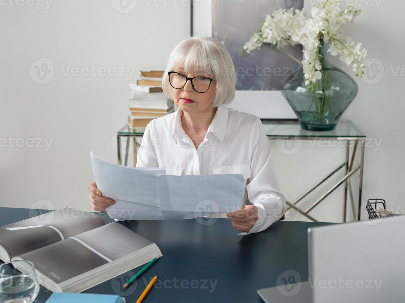 femme âgée fatiguée de beaux cheveux gris en blouse blanche lisant des documents au bureau. travail, personnes âgées, problèmes, trouver une solution, concept d'expérience photo