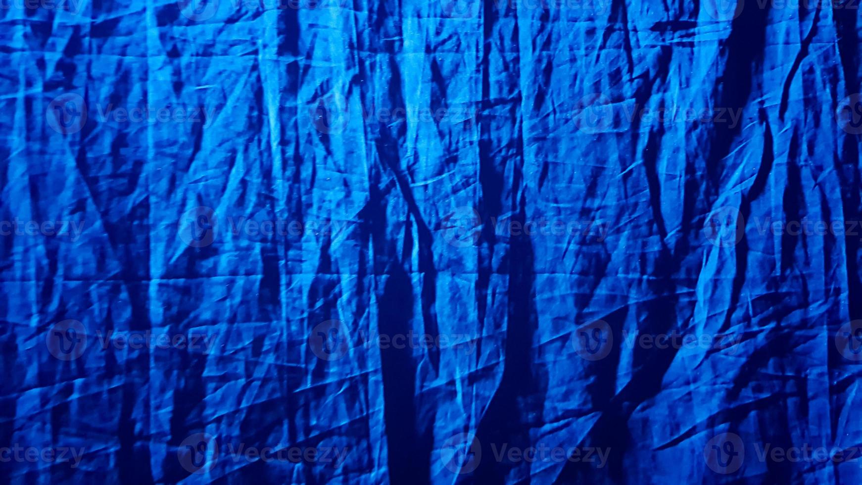 fond bleu en tissu pour votre conception. un rayon de lumière bleu illumine en diagonale le tissu dense, froissé et noir foncé. fond, motif, texture, papier peint. ajouter une touche de luxe à n'importe quel design photo