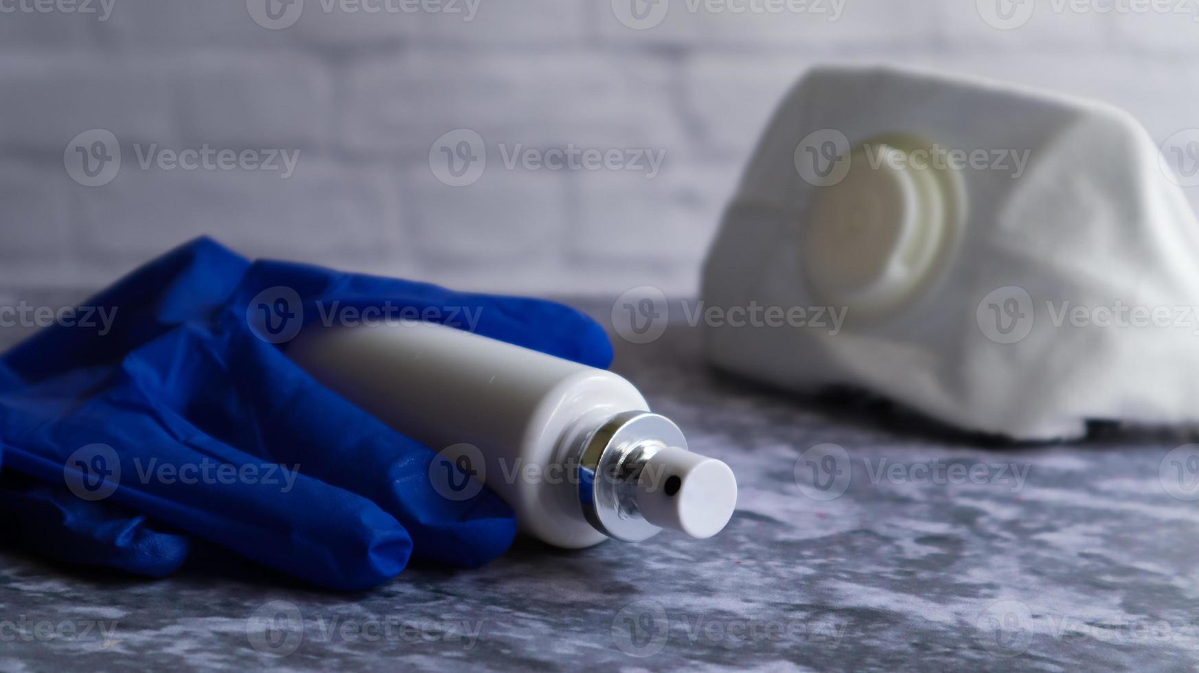 bouteille antiseptique blanche et masque d'un médicament protecteur sur une table grise, sur fond de mur de briques blanches. prévention de la maladie à coronavirus covid-19 lors d'une épidémie de virus de la grippe. photo