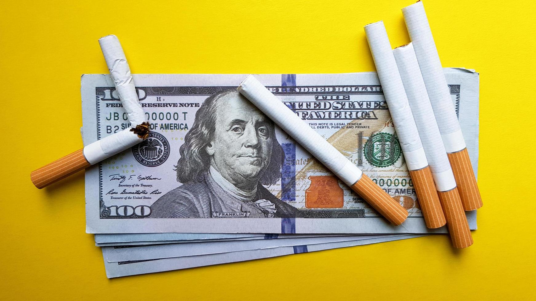 les cigarettes classiques se dressent sur des billets de cent dollars américains. cigarettes sur un billet de cent dollars sur fond jaune photo