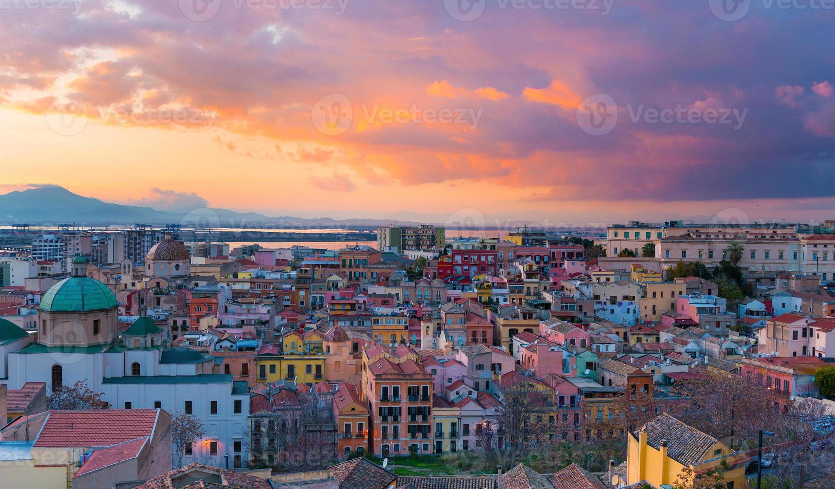 coucher de soleil sur cagliari, panorama sur la vieille ville avec des maisons colorées traditionnelles, des montagnes et de beaux nuages jaune-rose dans le ciel, sardaigne, italie photo