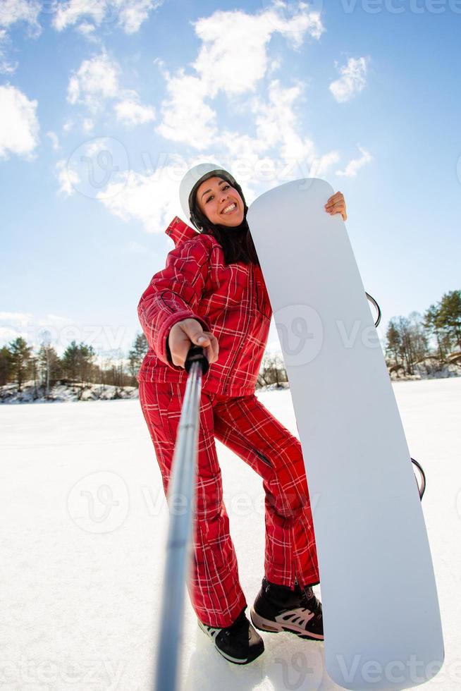 femme avec le snowboard utilisant un smartphone sur un bâton pour faire du selfie photo