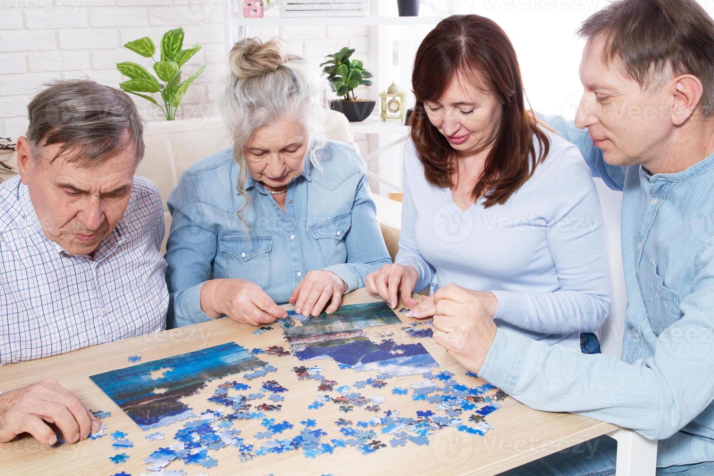 couple de personnes âgées résolvant un puzzle avec la famille à la maison. photo