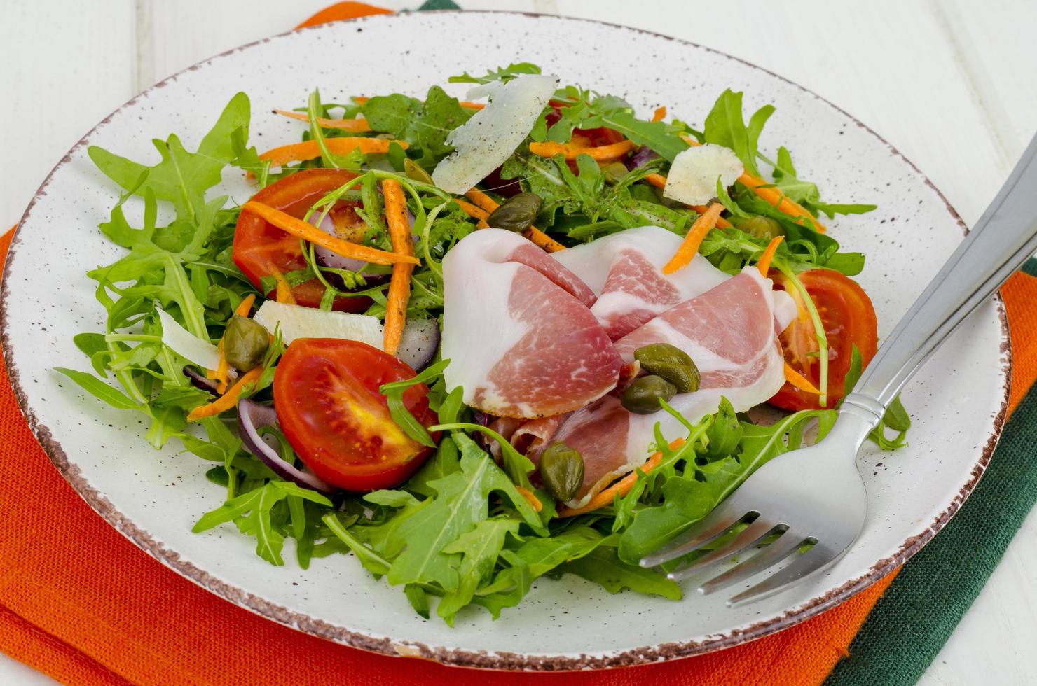 assiette avec des feuilles de salade fraîches, des tranches de parmesan et du jambon. studio photo