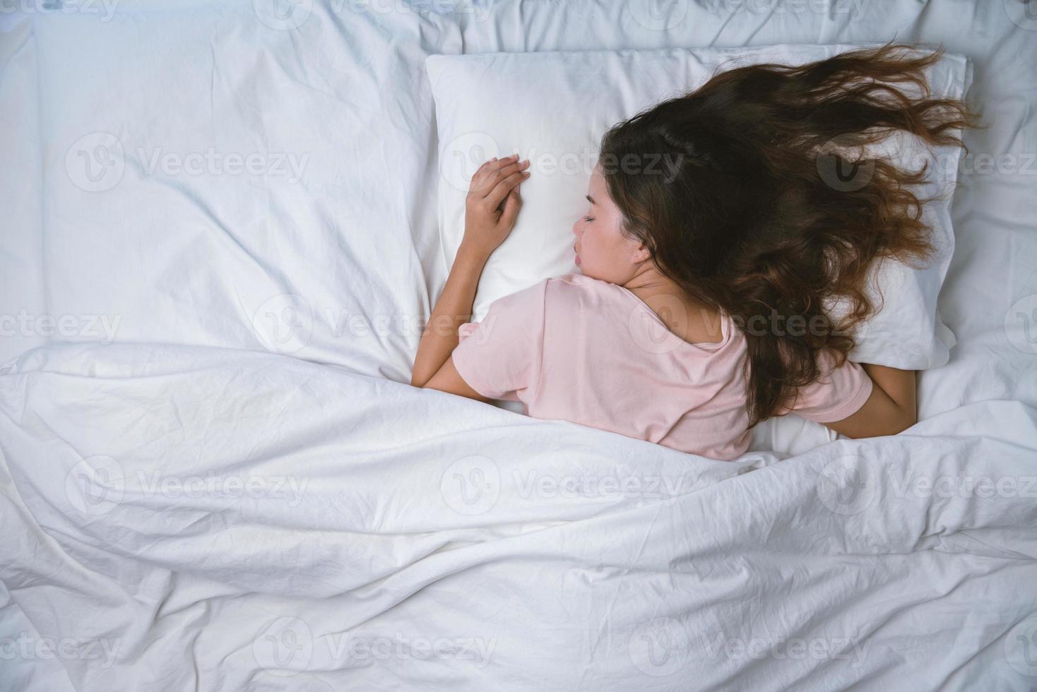 jeune femme dormant bien dans son lit étreignant un oreiller blanc doux. adolescente au repos. concept de bonne nuit de sommeil. une fille en pyjama dort sur un lit dans une pièce blanche le matin. ton chaud. photo