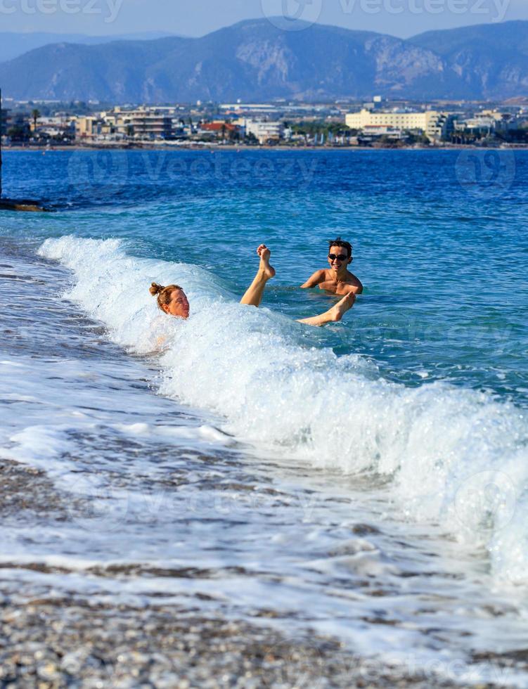 une vague côtière renverse une jeune femme qui entre dans la mer par une plage de galets. photo