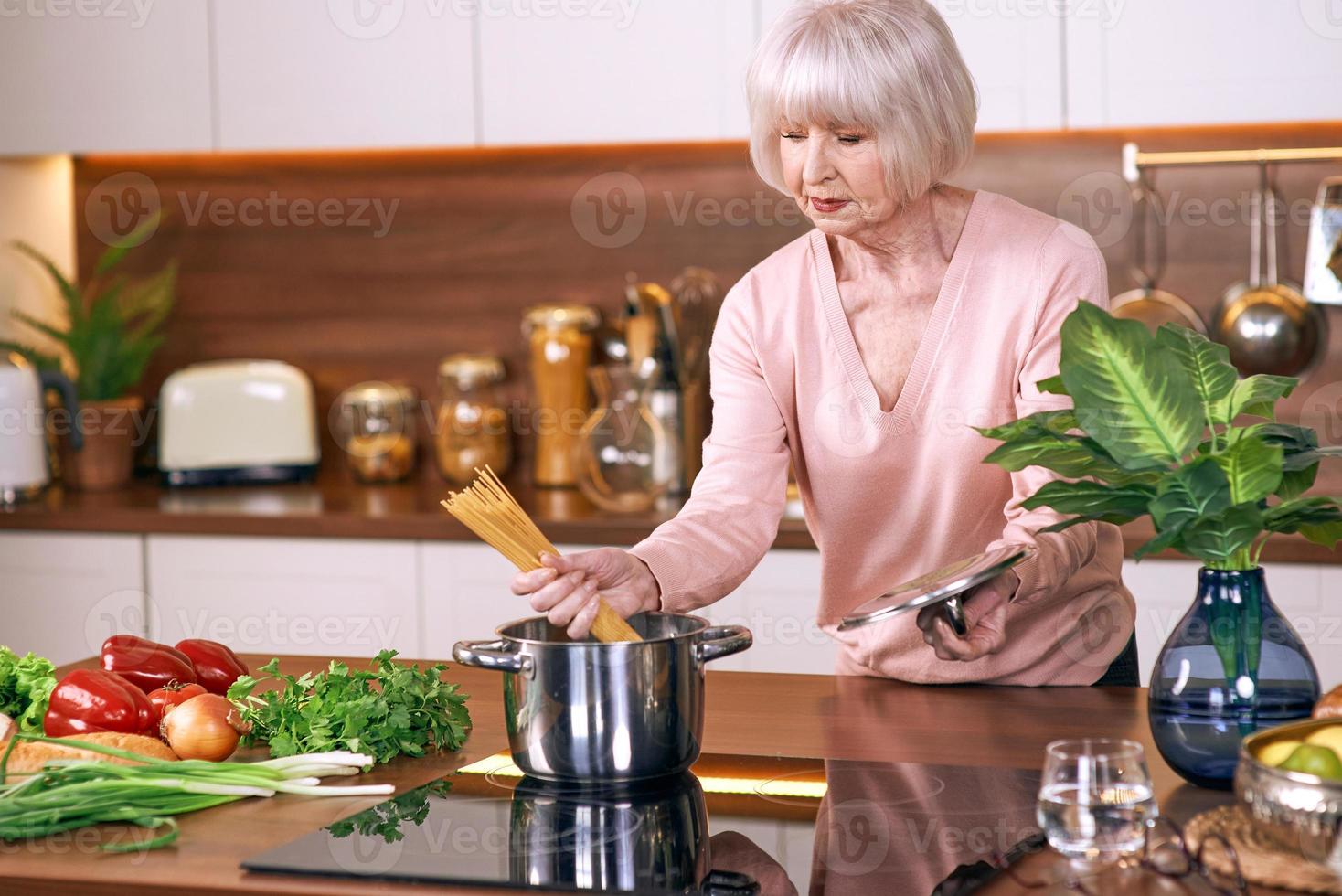femme joyeuse senior cuisine dans une cuisine moderne. nourriture, compétences, concept de mode de vie photo
