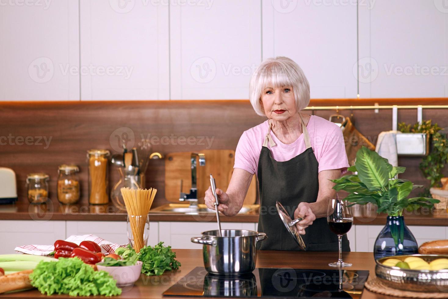 femme joyeuse senior cuisine dans une cuisine moderne. nourriture, compétences, concept de mode de vie photo