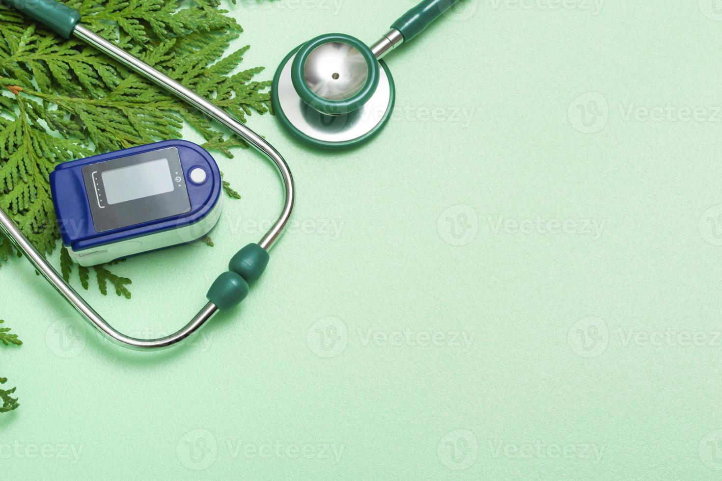 concept médical célébrant Noël dans les soins de santé. vue de dessus d'un gros plan à plat d'un stéthoscope, oxymètre de pouls avec des branches de sapin sur fond vert. photo