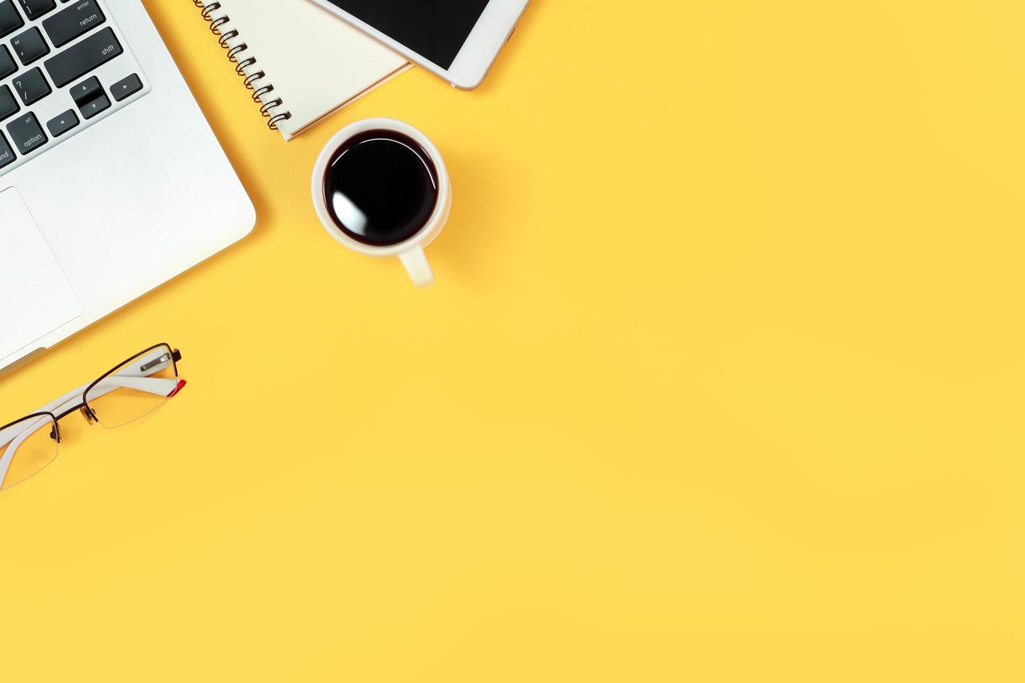 table d'espace de travail avec ordinateur portable, fournitures de bureau, tasse à café, téléphone portable et tasse à café sur fond jaune photo
