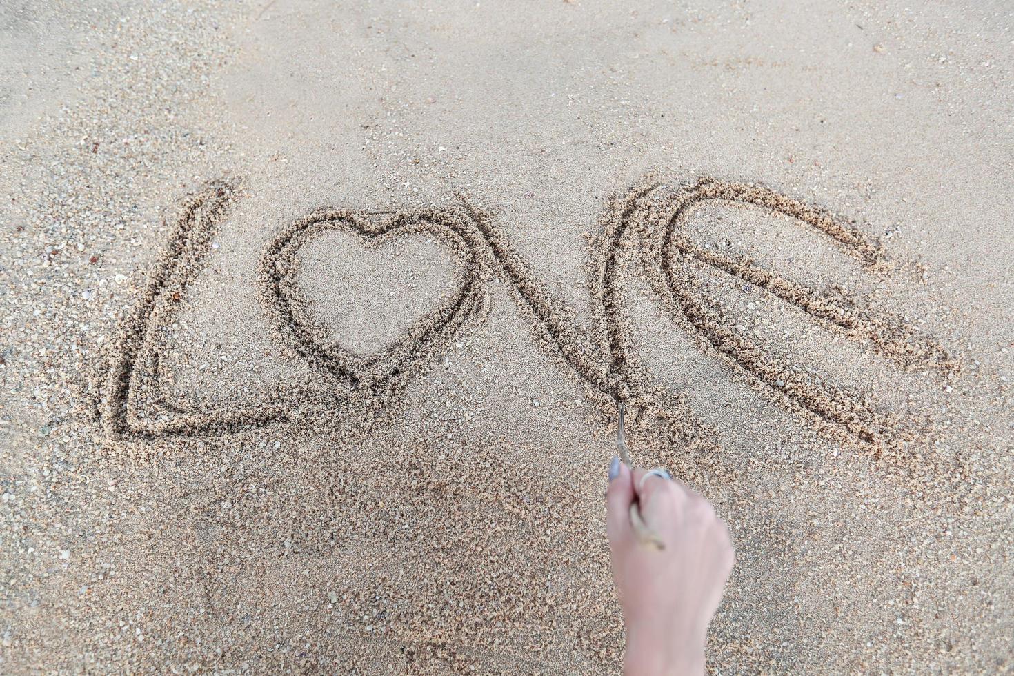 main de femme faisant le symbole du coeur et mot d'amour manuscrit sur la plage de sable photo