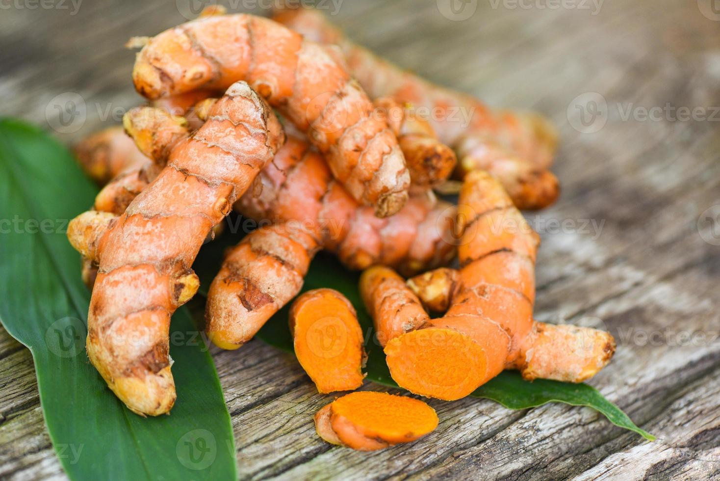 curcuma sur bois, racine de curcuma fraîche et feuilles vertes pour les herbes médicinales naturelles et les ingrédients cuits. photo