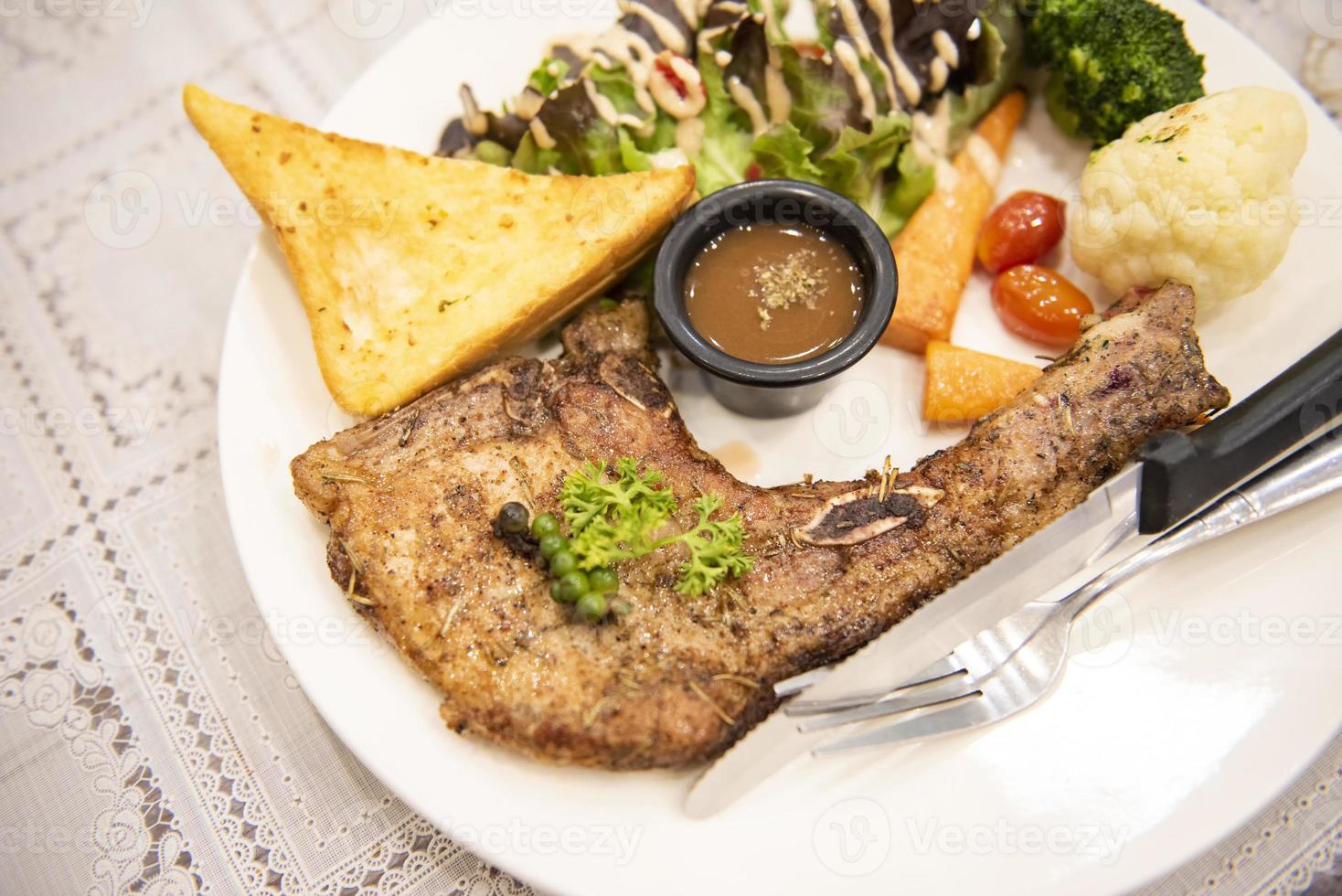 steak de porc rôti, côtelettes de porc grillées avec des épices aux herbes végétales maïs au poivre noir et pain grillé avec sauce à steak sur une assiette blanche sur la table à manger nourriture photo