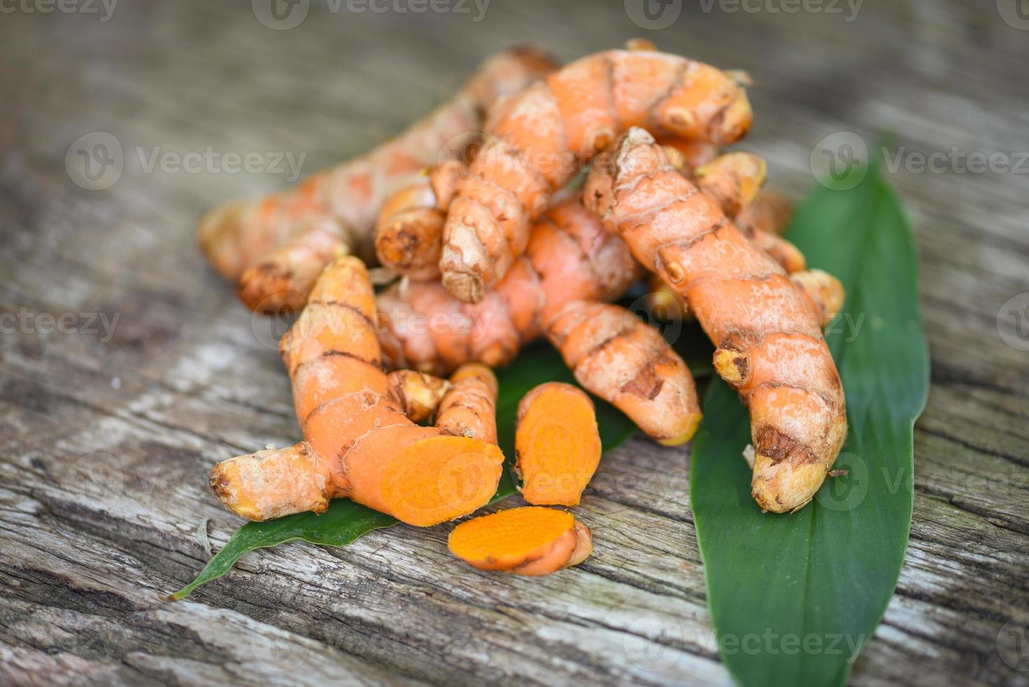 curcuma sur bois, racine de curcuma fraîche et feuilles vertes pour les herbes médicinales naturelles et les ingrédients cuits. photo