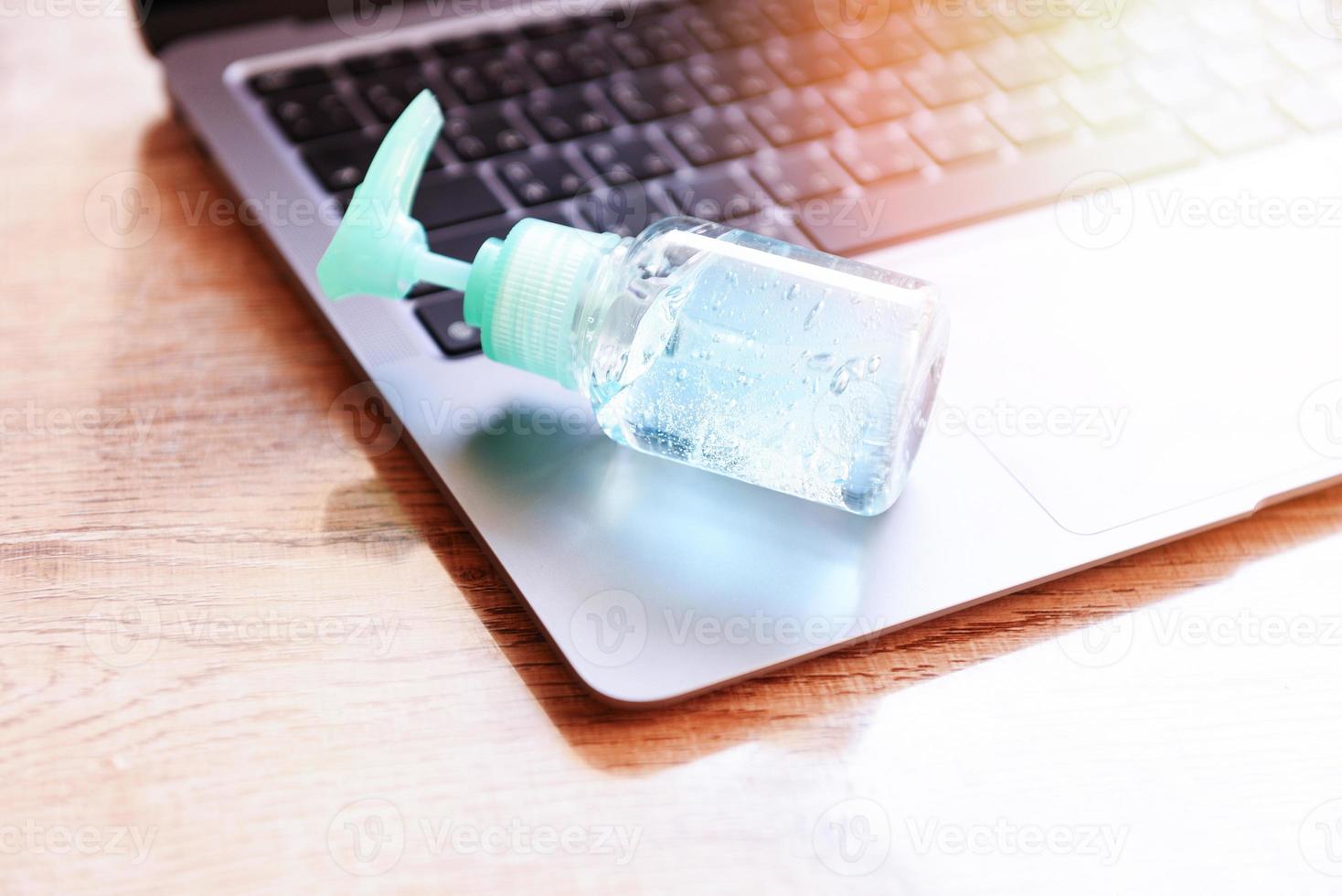 désinfecte la surface de l'ordinateur portable à l'aide d'un spray désinfectant ou d'un gel d'alcool lavant l'hygiène des mains sur le lieu de travail pour le coronavirus de quarantaine covid-19 travaillant à domicile. photo