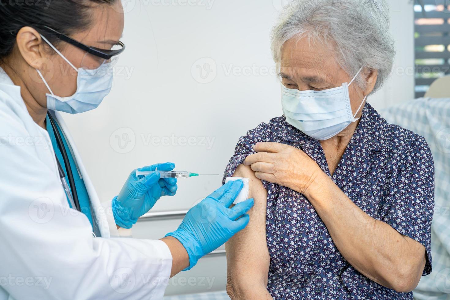 une femme âgée asiatique âgée portant un masque facial recevant un vaccin contre le covid-19 ou le coronavirus par un médecin fait une injection. photo