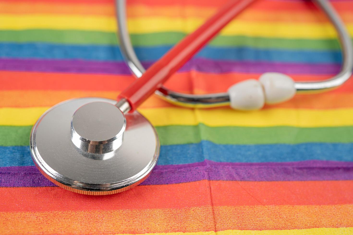 stéthoscope rouge sur fond de drapeau arc-en-ciel, symbole du mois de la fierté lgbt célèbre chaque année en juin social, symbole des gays, lesbiennes, bisexuels, transgenres, droits de l'homme et paix. photo