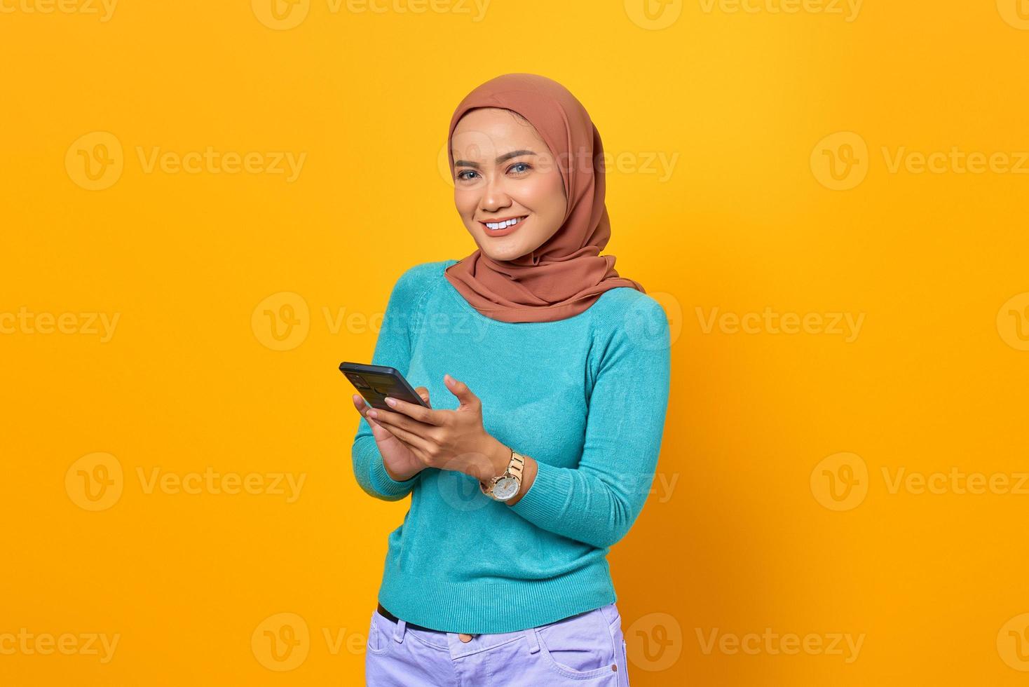 portrait de jeune femme asiatique souriante à l'aide d'un téléphone portable sur fond jaune photo