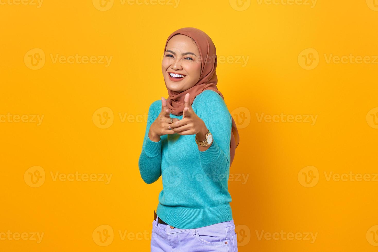 Souriante jeune femme asiatique pointant du doigt la caméra sur fond jaune photo