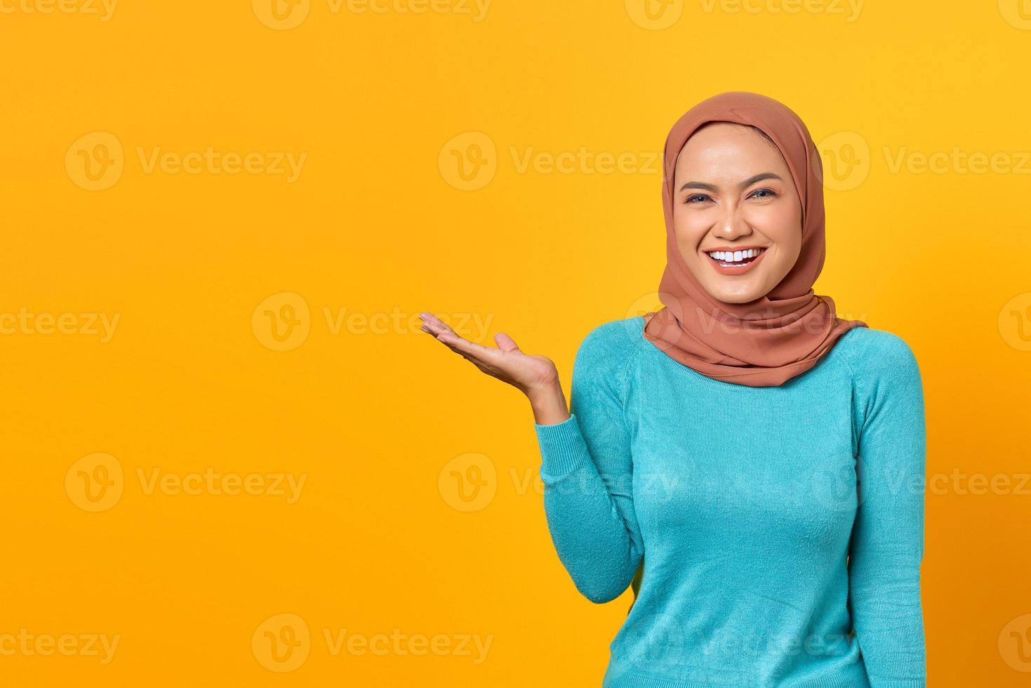 Portrait d'une jeune femme asiatique souriante montrant un espace de copie sur une paume isolée sur fond jaune photo