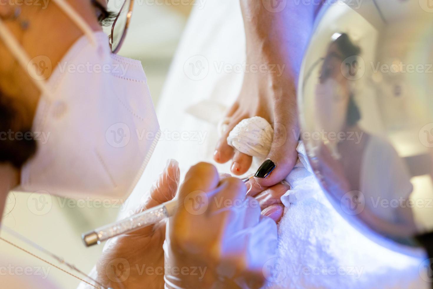 esthéticienne donnant une pédicure peignant les ongles de son client dans un centre de beauté. photo