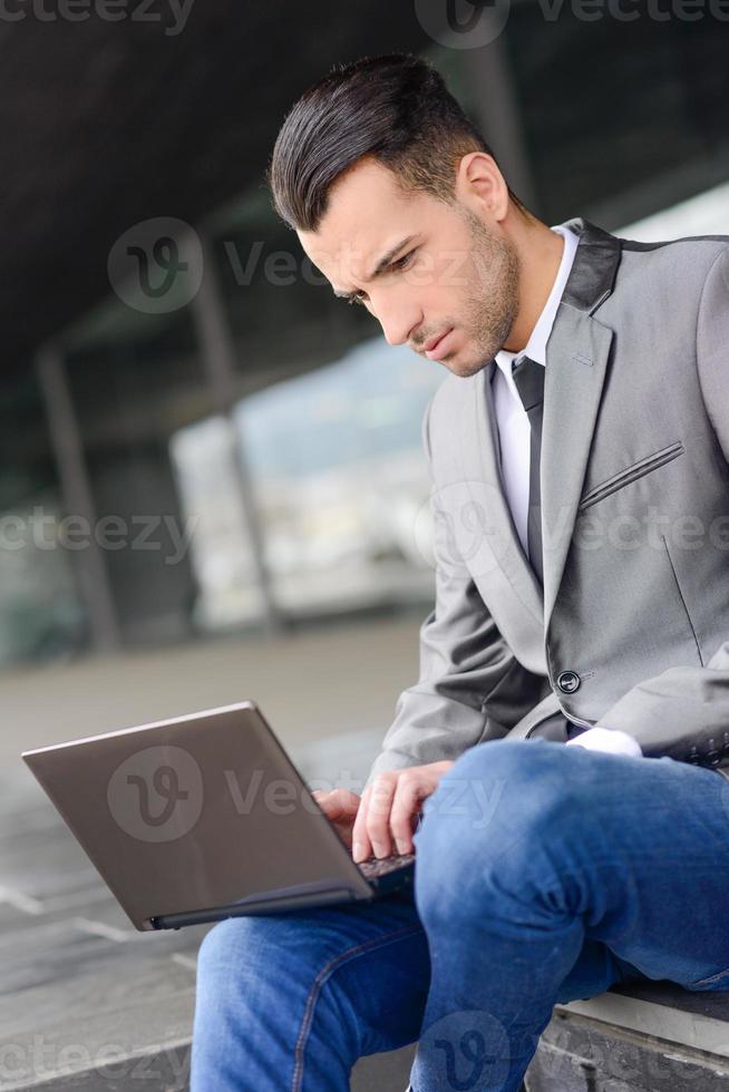 jeune homme d'affaires tapant dans un ordinateur portable en milieu urbain photo