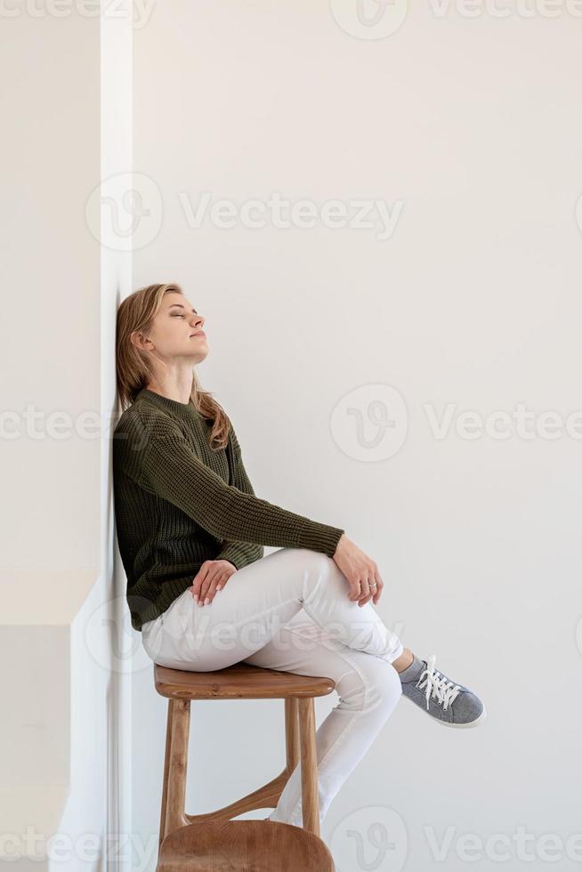 jolie jeune femme assise sur la chaise dans un intérieur clair et aéré avec les yeux fermés photo