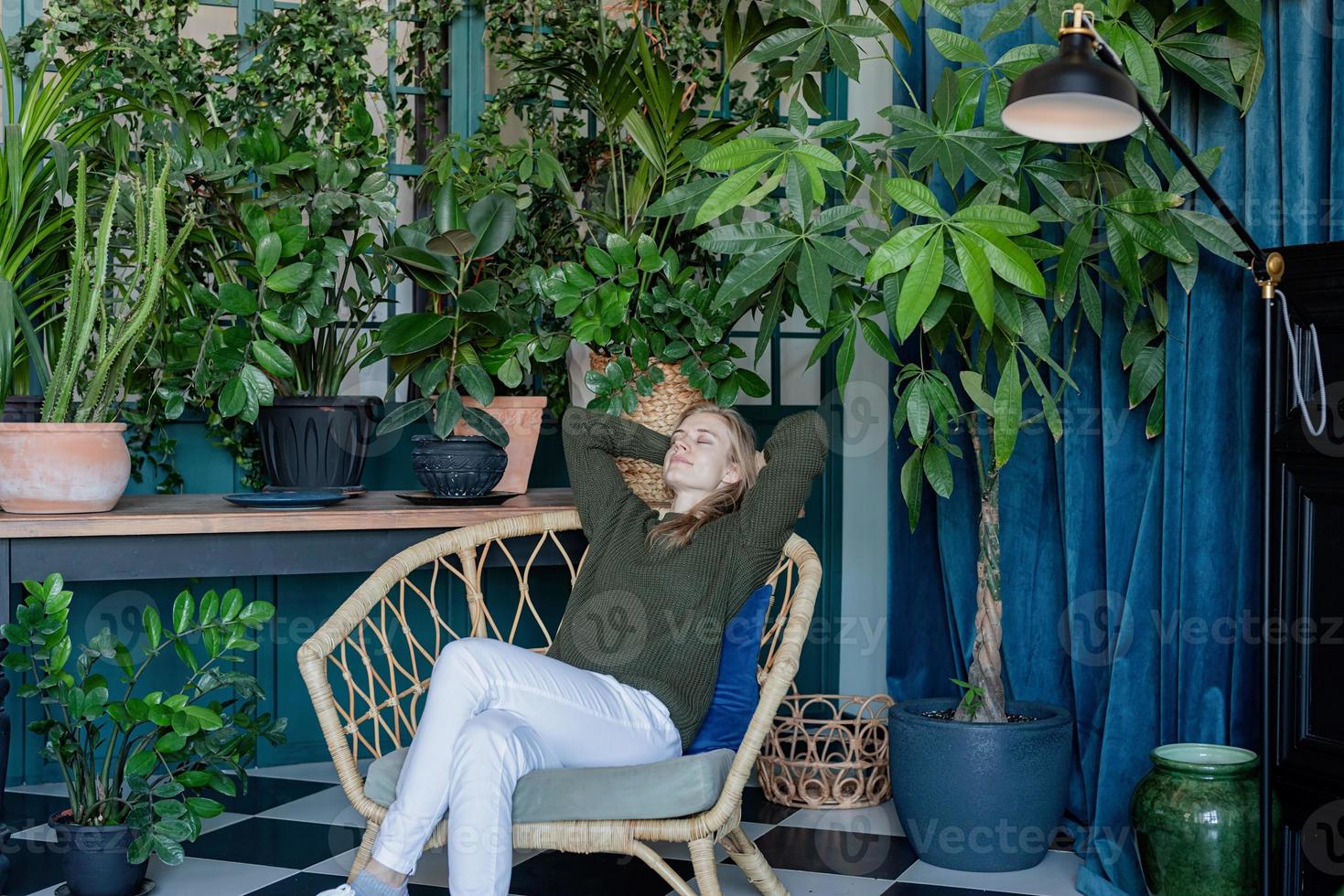 Jeune femme blonde assise sur une chaise confortable entourée de plantes photo