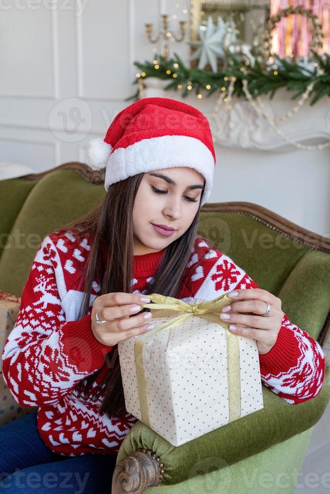 Jeune femme en pull rouge enveloppant un cadeau assis sur le canapé photo