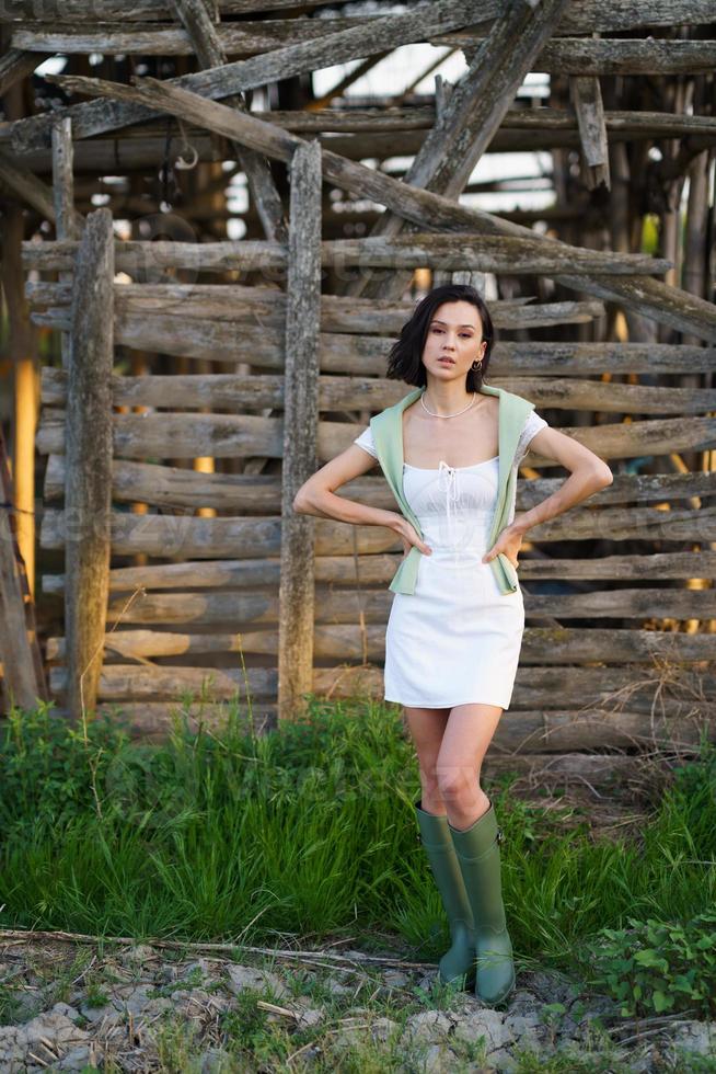 femme asiatique, posant près d'un séchoir à tabac, vêtue d'une robe blanche et de bottes en caoutchouc vertes. photo