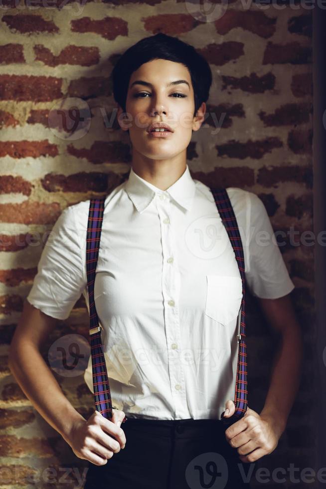 belle jeune femme avec une coupe de cheveux très courte, regardant la caméra avec un mur de briques en arrière-plan. photo