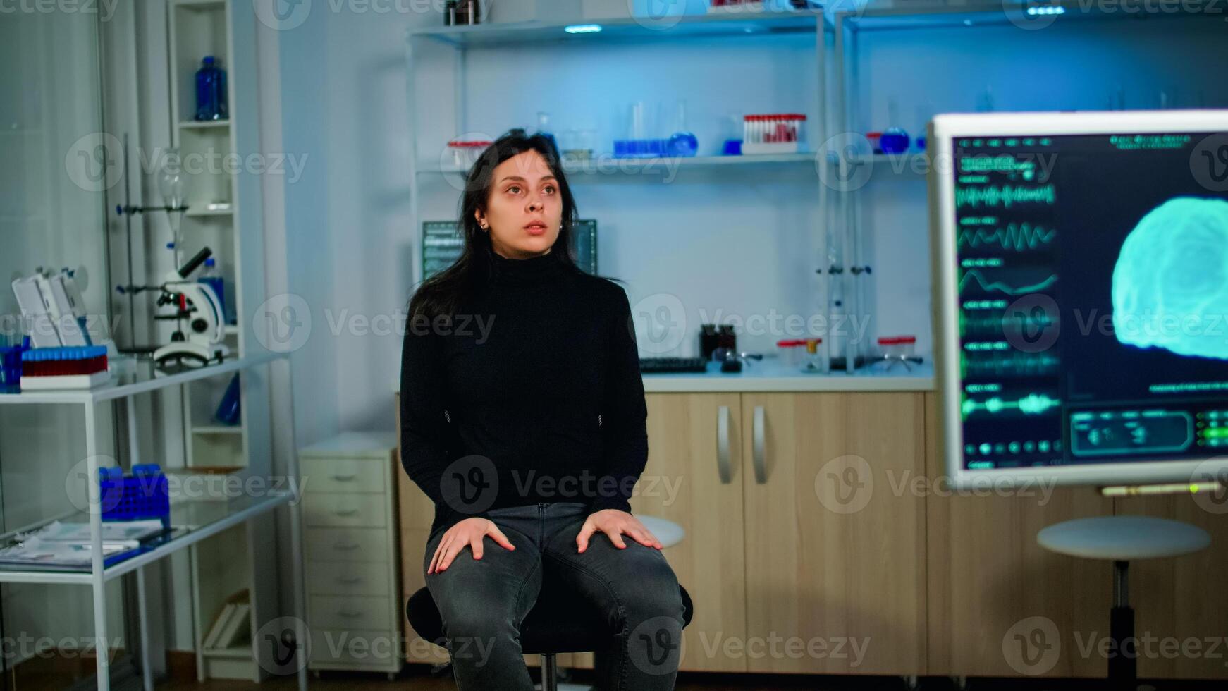 stressé patient séance sur chaise dans neurologique laboratoire attendre pour médical chercheur enquêter cerveau les fonctions en utilisant haute technologie et neurologie outils. nerveux système analyse montrant sur moniteur photo