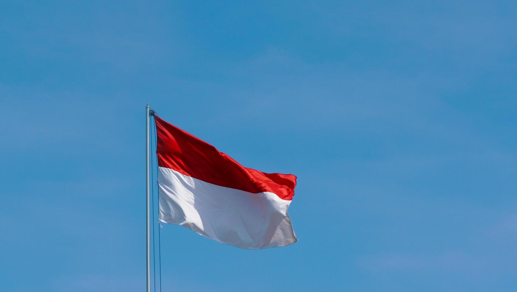 le drapeau indonésien flotte haut. le drapeau ondulant avec un fond de ciel bleu clair. le drapeau rouge et blanc agitant fièrement un jour ensoleillé. photo