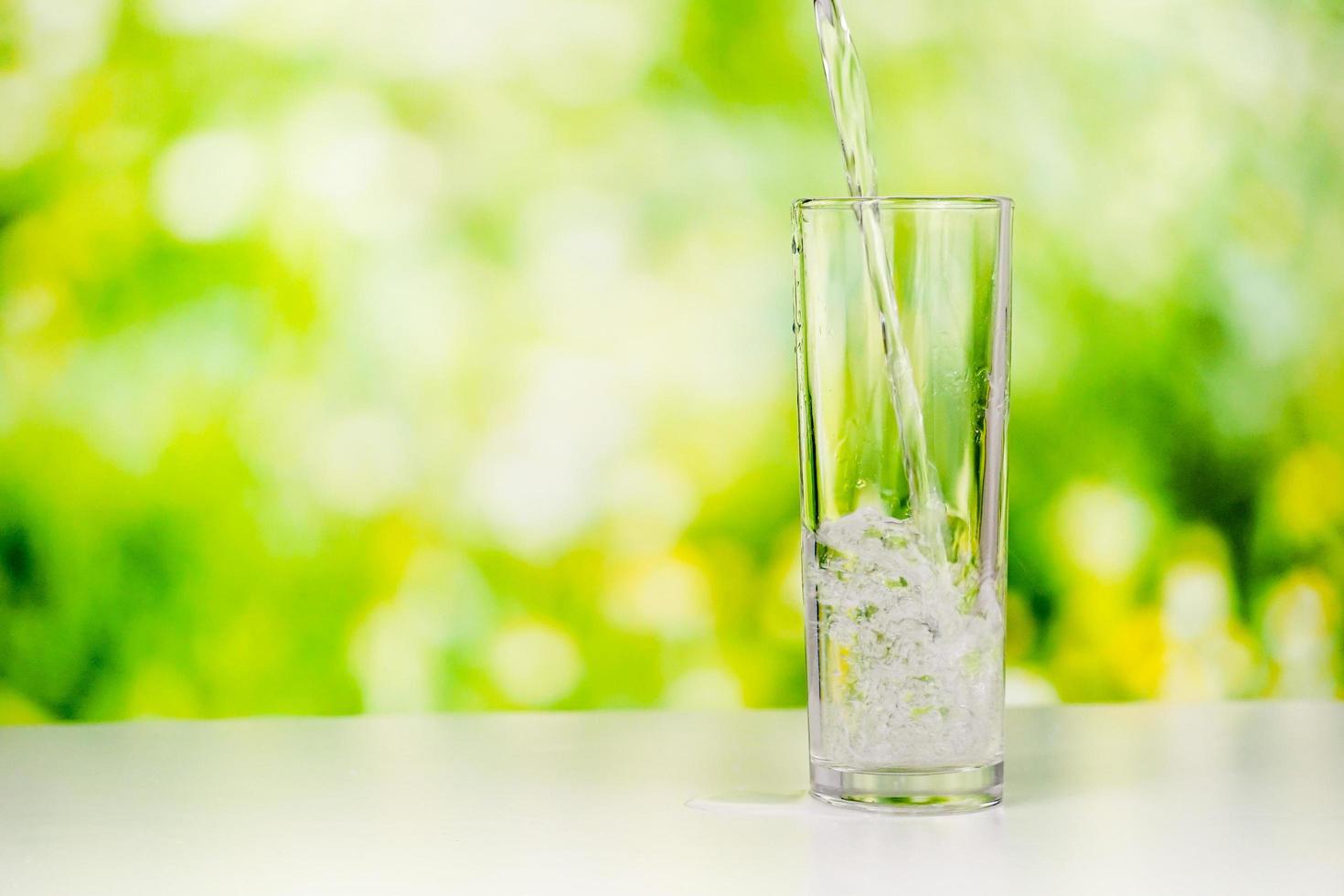 verser de l'eau pure dans un grand verre transparent sur le bureau avec un fond de verdure. un tournage en studio d'eau qui coule. photo