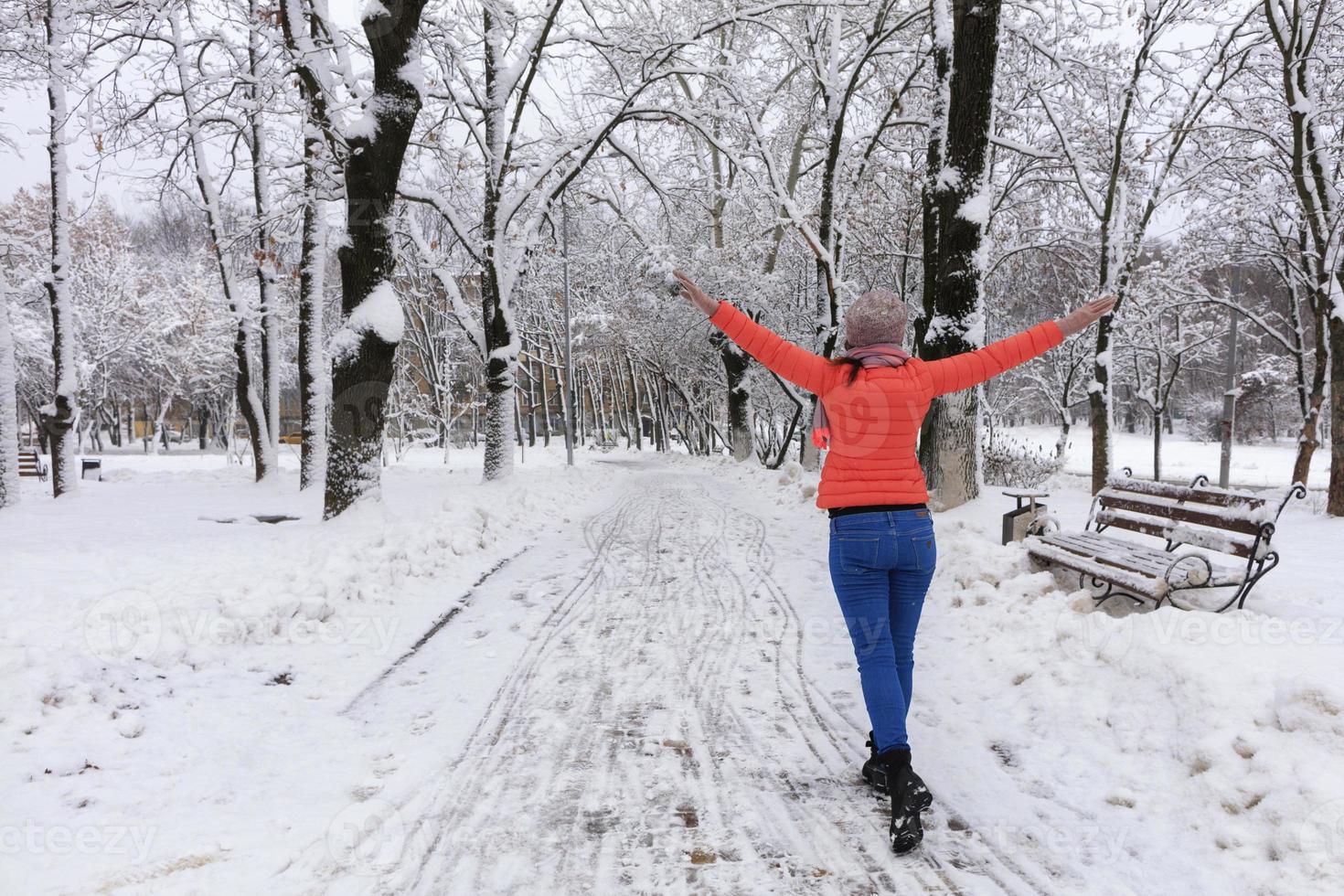 une belle jeune femme marche en hiver le long d'une ruelle dans un fabuleux parc enneigé de la ville avec ses bras écartés comme des ailes photo