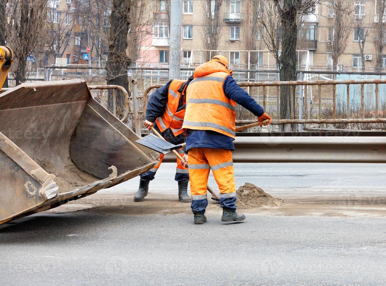 les ouvriers routiers utilisent des pelles pour gratter le sable accumulé entre les voies de la route et le charger dans le godet de la niveleuse. photo