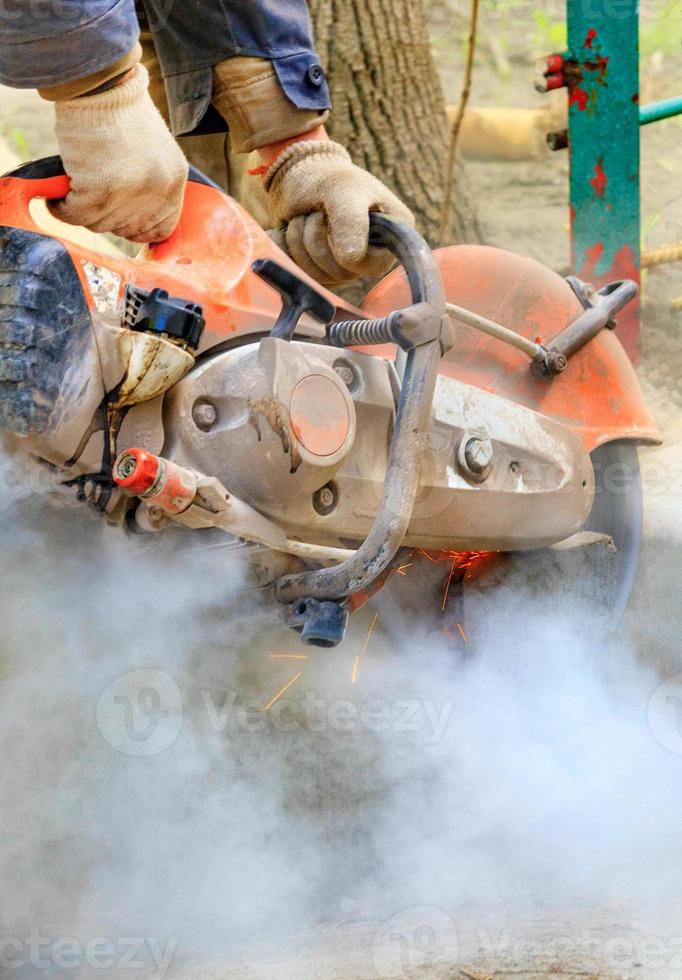 un constructeur utilise un cutter portable pour découper une structure en béton dans un nuage de poussière. photo