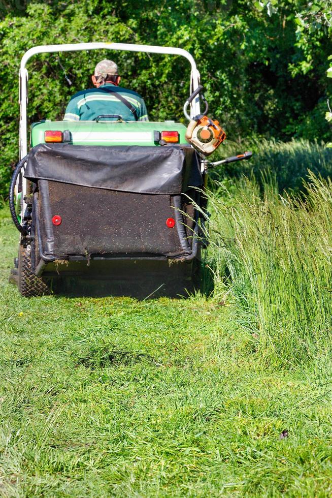 un jardinier tond les hautes herbes vertes et les ramasse dans la trémie d'une tondeuse à gazon professionnelle. l'arrière-plan est légèrement flou. photo