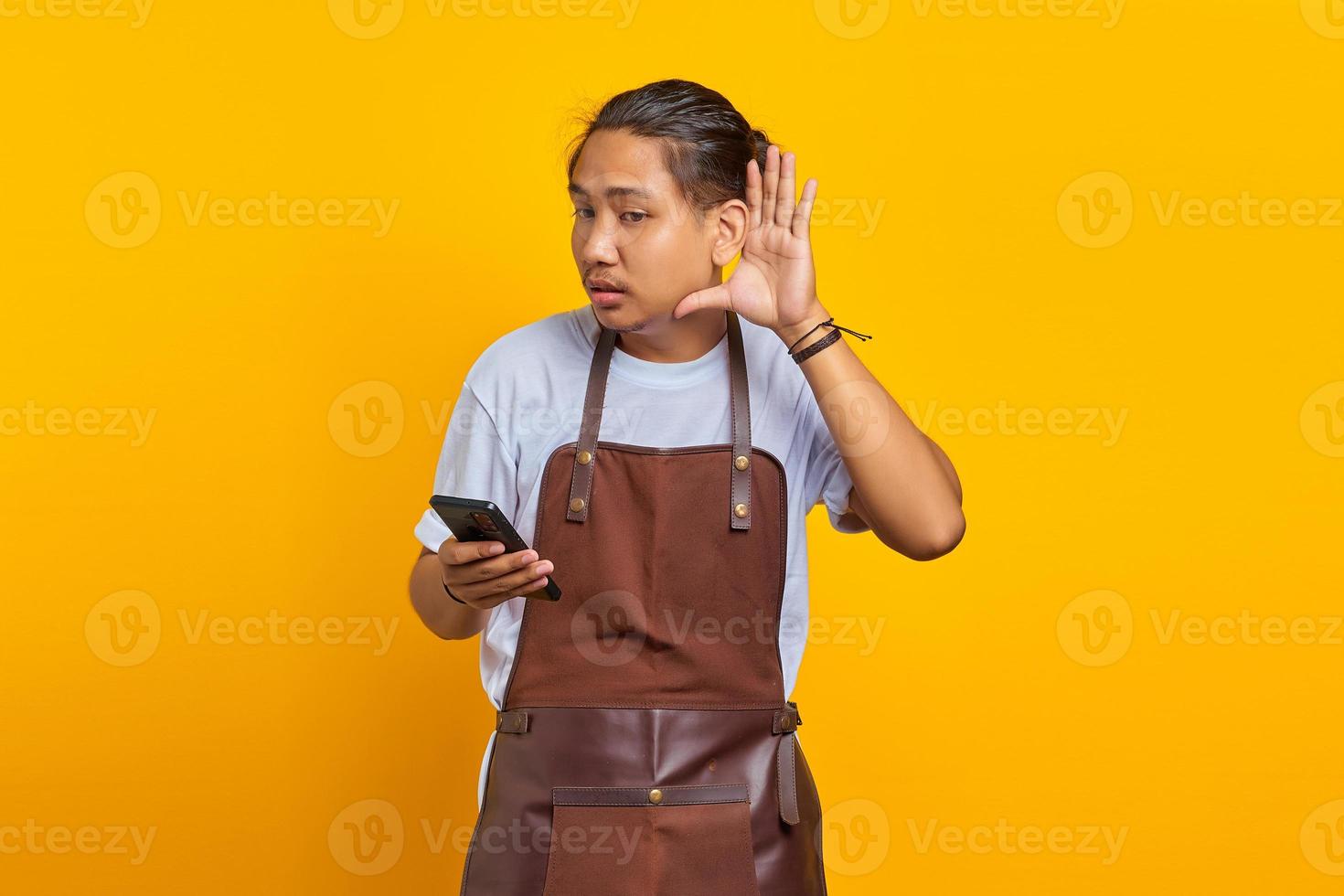 portrait d'un homme asiatique sérieux essayant d'entendre une conversation secrète et tenant un smartphone photo