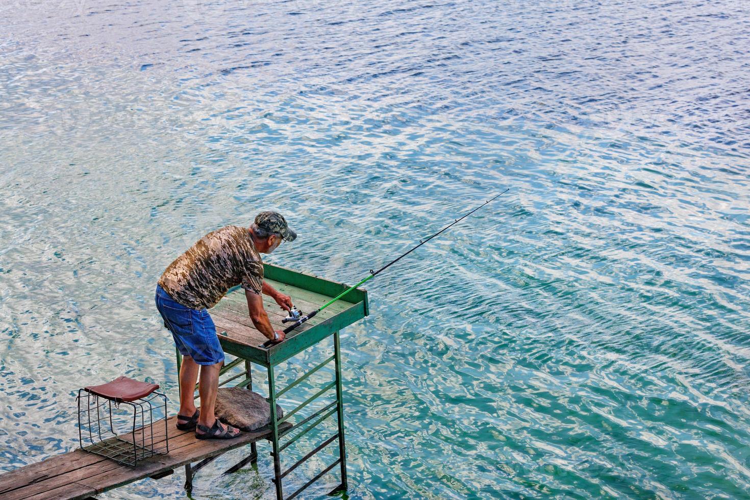 un pêcheur pêche en filant au bord de la rivière, debout sur une plate-forme en bois. photo