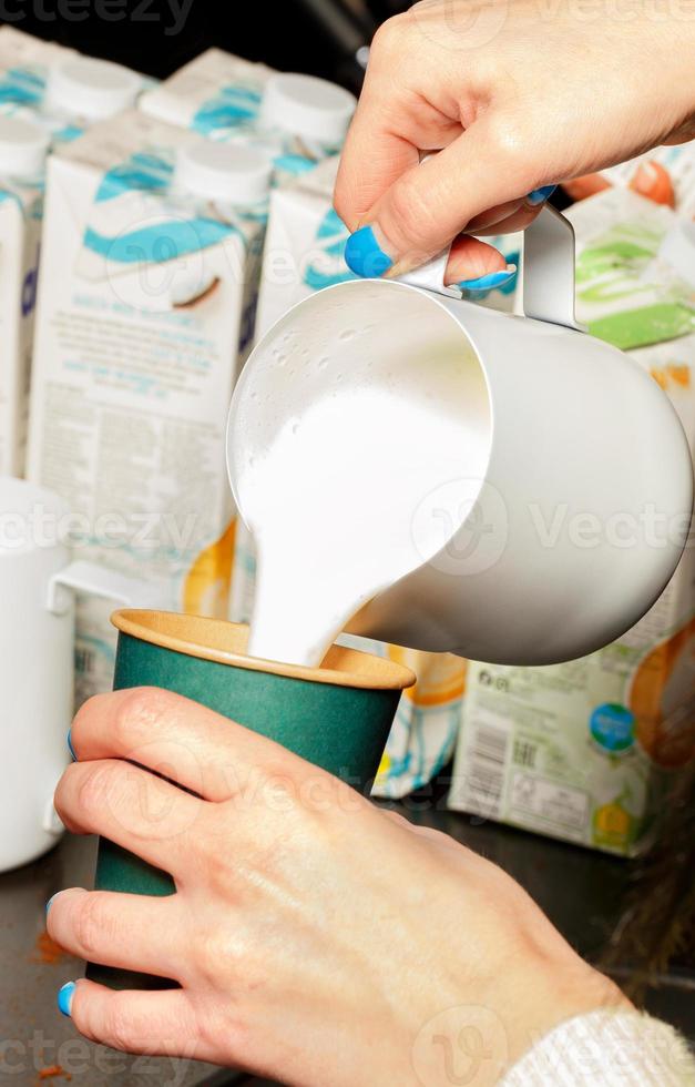 le barista verse de la crème fouettée mousseuse dans une tasse à café en papier vert. photo